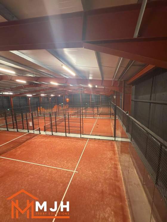 Indoor padel courts with structural steelwork sprayed deep terracotta red